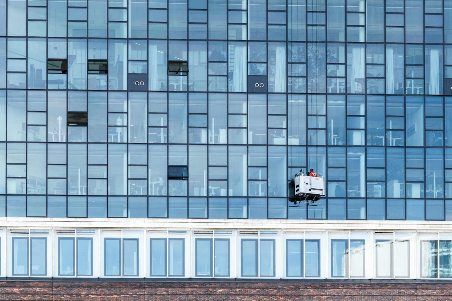 Glazenwasser op een hangende gondel wast een modern gebouw.